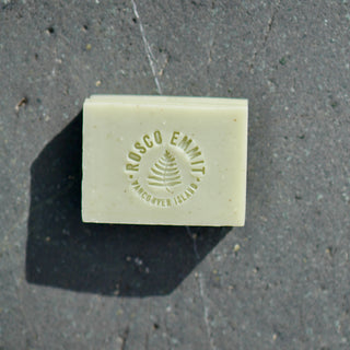 A rectangular bar of pale cream-colored soap with 'ROSCO EMMIT' and 'VANCOVER, ILLINOIS' embossed on the top, placed on a dark textured stone surface.
