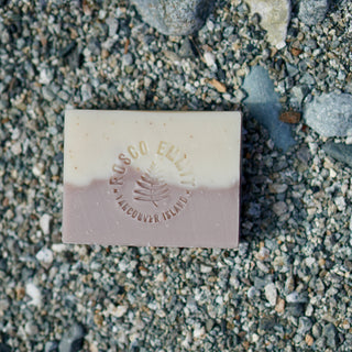A rectangular bar of Rosco Elliott Vancouver Island soap, featuring a cream top half and a dusty mauve-pink bottom half, embossed with the brand name and a pine tree logo, resting on a bed of gray and white gravel.
